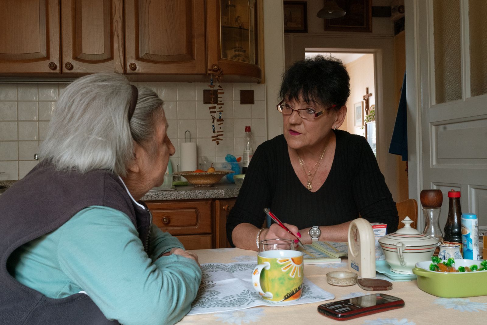 Eine Pflegekraft im ruhigen Gespräch mit einer älteren Frau in ihrem Wohnzimmer